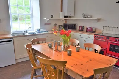a kitchen with a wooden table with flowers on it at Coachmans Cottage in Carsethorn