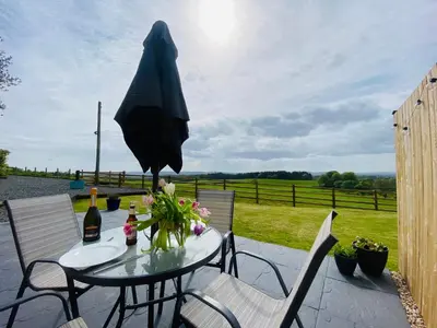 a patio with a table with a bottle of wine and a umbrella at Cleugh Lodge in Lockerbie