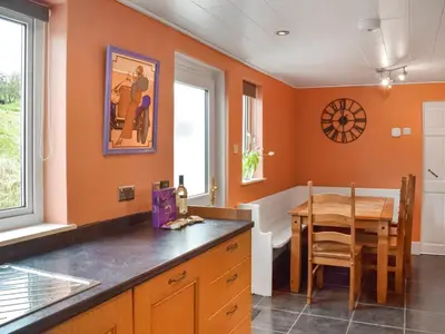 a kitchen with orange walls and a wooden table at Winlocke Cottage in Leadhills