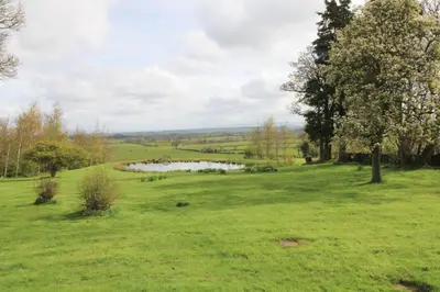 a grassy field with a pond in the distance at Cloven Stone, Nr Caldbeck ideal family accommodation with hot tub in Sebergham