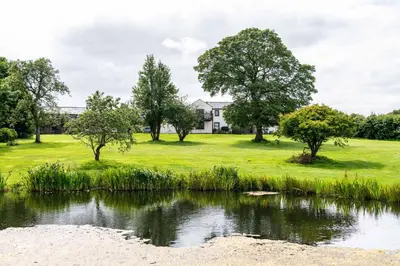 a house in a field with a pond at Fisher Gill, Sebergham, Close to Caldbeck Fells with hot tub in Sebergham