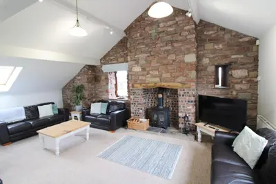 a living room with a stone wall with a fireplace at Great Calva, Sebergham, perfect for 2 families or friends with 3 dogs welcome and hot tub in Sebergham