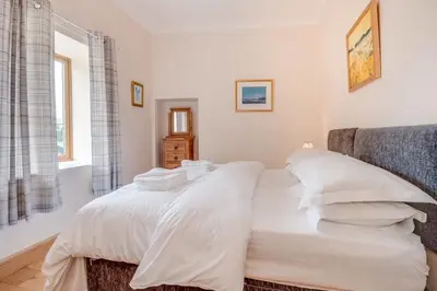 a bedroom with a bed with white sheets and pillows at Kinnen Cottage in Creetown