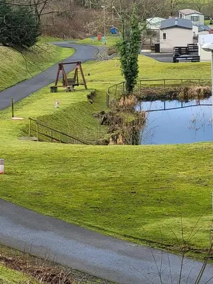 a park with a playground and a pond at The Sunny Bunny Holiday Home in Ballantrae