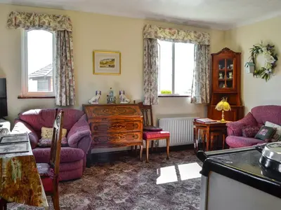 a living room with purple chairs and a table and windows at Rose Rigg Cottage in Kirklinton