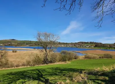 a grassy field with a lake in the background at Strathken Cottage in Castle Douglas