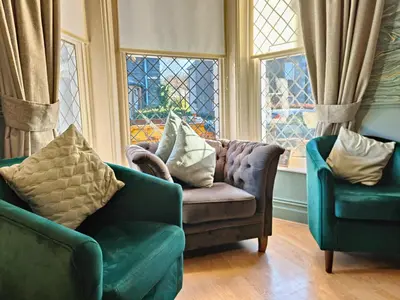 a living room with two chairs and a couch and windows at Squirrel Lodge in Keswick