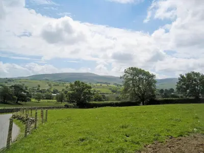 a green field with trees and mountains in the distance at Ellarbeck Cottage in Caldbeck