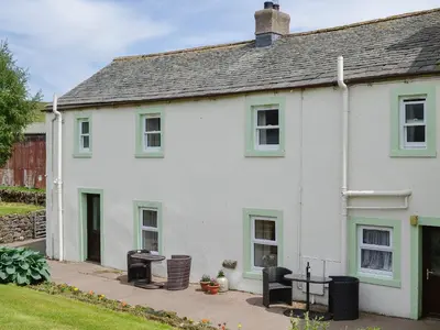 a white house with green windows and a patio at Swaledale Cottag in Caldbeck