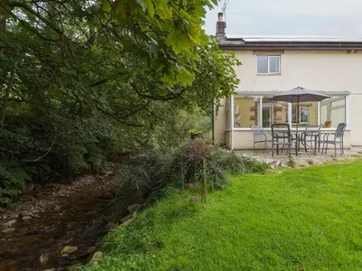 a house with a table and chairs and an umbrella at Beck Cottage in Ennerdale Bridge