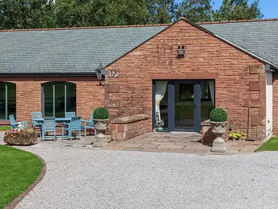 a brick building with a patio with blue chairs at Beckside in Gilcrux