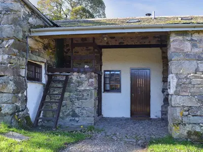 an old stone building with a wooden door and a ladder at Birkerthwaite Barn-W41478 in Eskdale