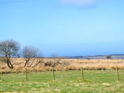 a fence in a field with trees in the background at Stonefold Cottage in Waberthwaite
