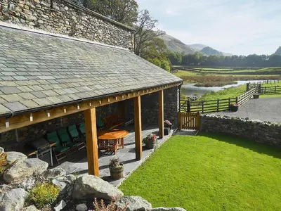 a stone building with a table and chairs next to a river at Bram Crag Barn in Legburthwaite