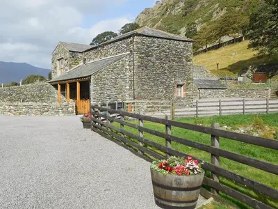 a stone building with a fence and flowers in a barrel at Bram Crag Barn in Legburthwaite