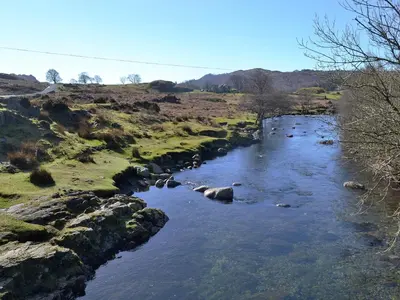 a river with rocks in the middle of a field at Whistling Green in Ulpha