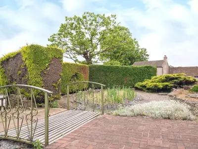 a garden with a metal gate and a brick walkway at Oaklands in Langrigg