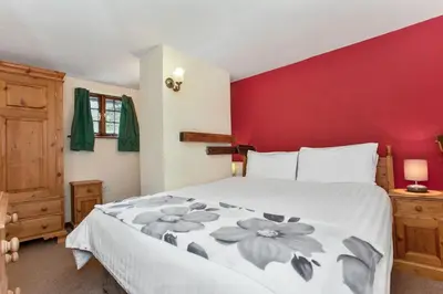 a bedroom with a large bed with a red wall at The Coppermines Mountain Cottages - Carpenters, Millrace, Pelton Wheel, Sleeps 14 in Coniston