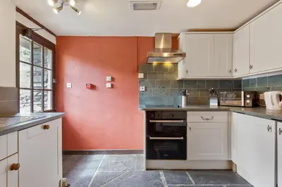 a kitchen with white cabinets and a red wall at The Coppermines Mountain Cottages - Carpenters, Millrace, Pelton Wheel, Sleeps 14 in Coniston
