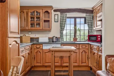 a kitchen with wooden cabinets and a table at The Coppermines Mountain Cottages - Sawyers, Carpenters, Pelton Wheel, Sleeps 18 in Coniston