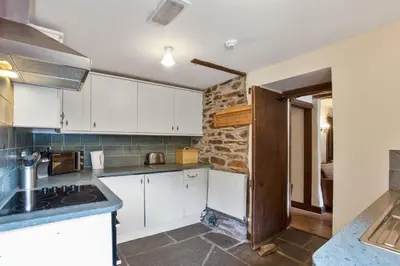 a kitchen with white cabinets and a stone wall at The Coppermines Mountain Cottages - Sawyers, Carpenters, Pelton Wheel, Sleeps 18 in Coniston