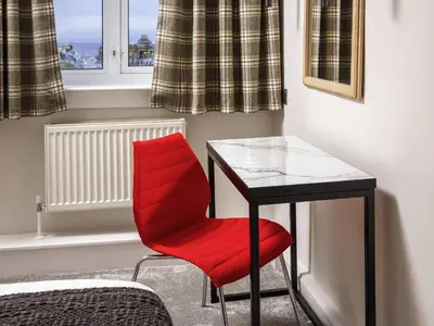 a red chair sitting next to a desk in a room at Mercure Ayr Hotel in Ayr