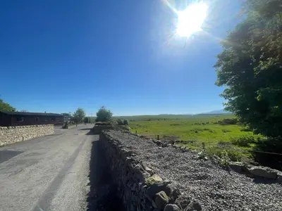 a road with a stone wall and the sun in the sky at Lake District Luxury Lodge in Plumbland