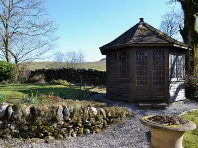 a small building in a garden with a stone wall at Arkland Mill in Corsock