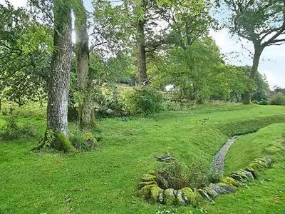 a grassy field with a tree and a rock circle at Marwhin House - Swwr in Kirkpatrick Durham