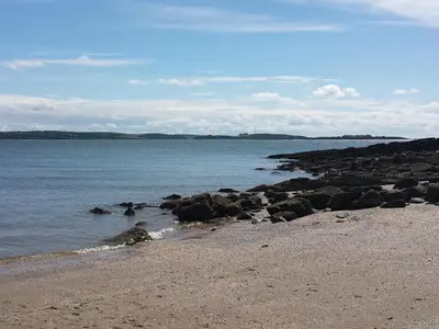 a beach with rocks and the ocean on a cloudy day at Burnbank in Kirkgunzeon