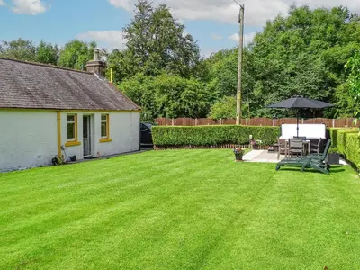 a yard with a house and an umbrella at Blaeberry Cottage - 28061 in Dinwoodie Mains