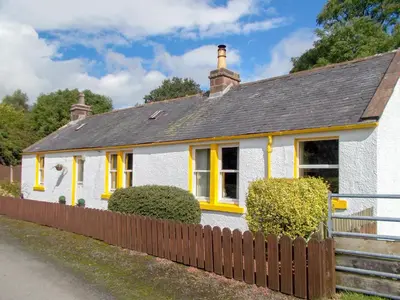 a white house with yellow windows and a fence at Blaeberry Cottage - 28061 in Dinwoodie Mains