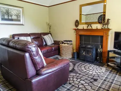 a living room with a leather couch and a fireplace at Blaeberry Cottage - 28061 in Dinwoodie Mains
