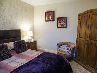 a bedroom with a large bed and a chair at Blaeberry Cottage - 28061 in Dinwoodie Mains