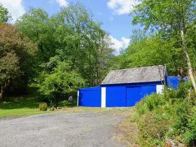 a blue and white shed next to a gravel road at Little Boreland in Gatehouse of Fleet