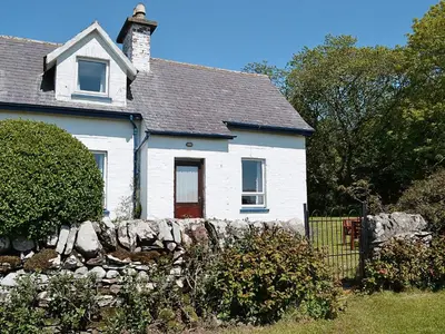 a white house with a stone fence in front of it at Olafs Cottage in Garlieston