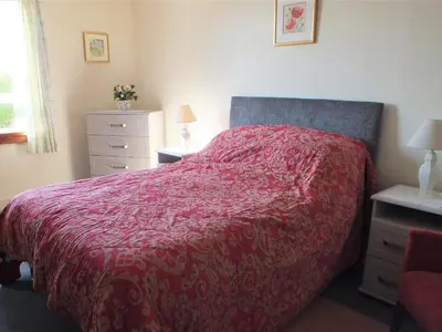 a bedroom with a bed with a red comforter at Olafs Cottage in Garlieston