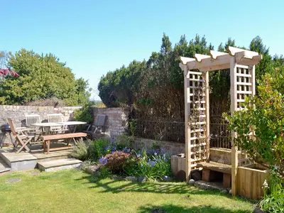 a garden with a wooden pergola and a table at The Cottage in Garlieston