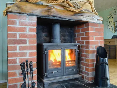 a brick fireplace with a fire in it at Driftwood in Mainsriddle