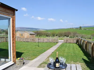 a bottle of wine and glasses on a table in a yard at Rose Cottage - 28176 in Fairgirth