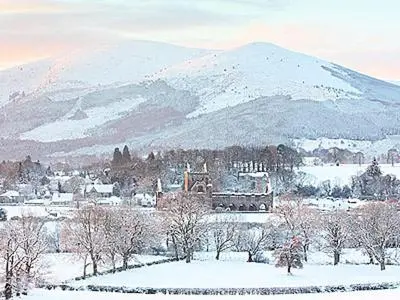 a snow covered mountain in front of a town with a building at Myrtle Cottage - 28177 in Fairgirth