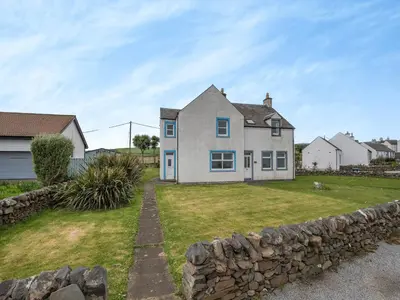 a house with a stone wall in front of a yard at Jura in Drummore