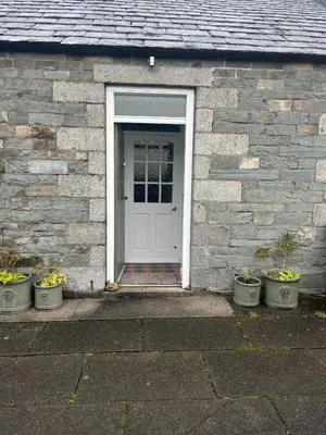 a white door of a brick house with potted plants at Apple Cottage in Wigtown