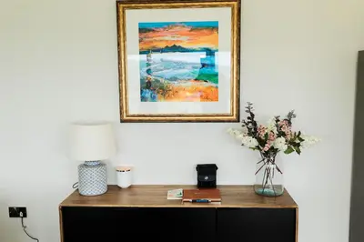 a table with a vase of flowers and a picture on the wall at Cairn Dyke Lodge in Gatehouse of Fleet