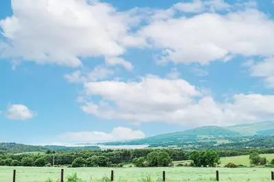a field with a fence and a blue sky with clouds at Cairn Dyke Lodge in Gatehouse of Fleet