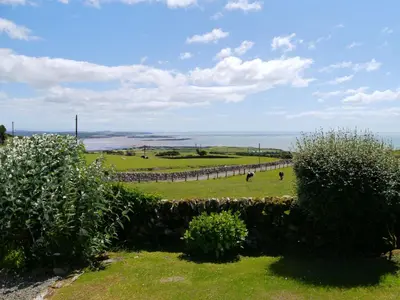a view of a field with a fence and the ocean at High Auchenlarie Cottage in Gatehouse of Fleet