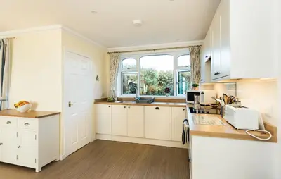 a kitchen with white cabinets and a window at High Auchenlarie Cottage in Gatehouse of Fleet