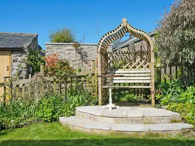a wooden bench in a garden with a fence at Earsdon Cottage in Ireby