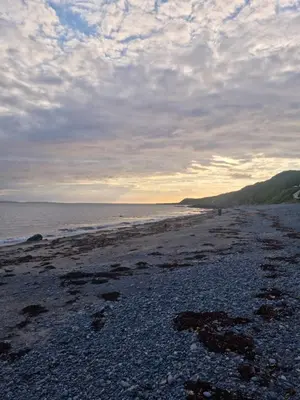 a beach with a cloudy sky and the ocean at Serenity in Monreith