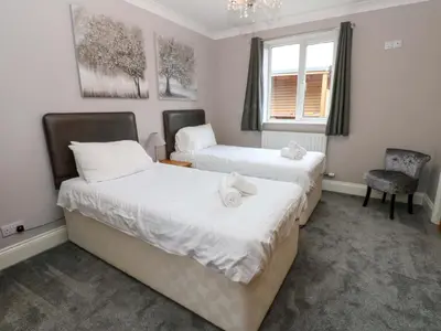 two beds in a room with a window and a chair at Fern Lee in Carlisle